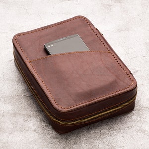 May include: A brown leather zipped case with a black phone inside. The case has a pocket on the front for the phone.