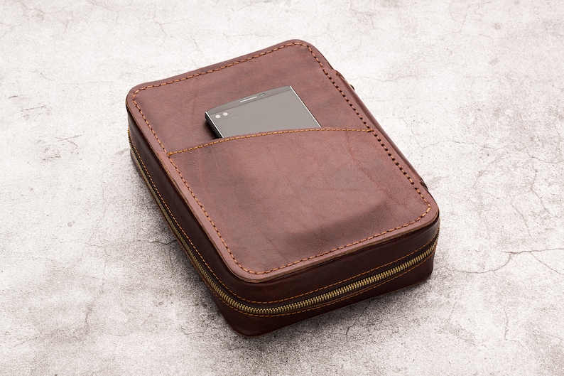 May include: A brown leather zipped case with a black phone inside. The case has a pocket on the front for the phone.
