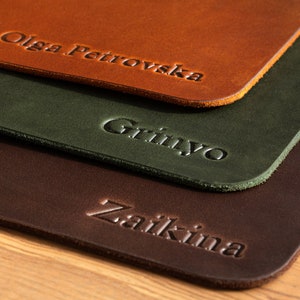 May include: Three leather coasters with names embossed on them. The top coaster is orange and says "Olga Petrovska". The middle coaster is green and says "Grinyo". The bottom coaster is brown and says "Zaikina".
