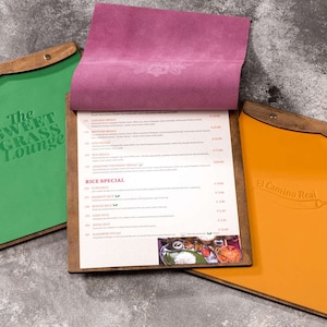 May include: Three wooden menu boards with leather covers. The first board is green and says "The Sweet Grass Lounge". The second board is pink and has a menu for "Rice Special". The third board is orange and says "El Camino Real".