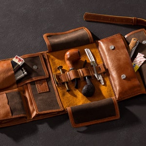 May include: A brown leather tobacco pouch with multiple compartments. The pouch is open and contains a pipe, a pipe tamper, a lighter, matches, and a small knife.