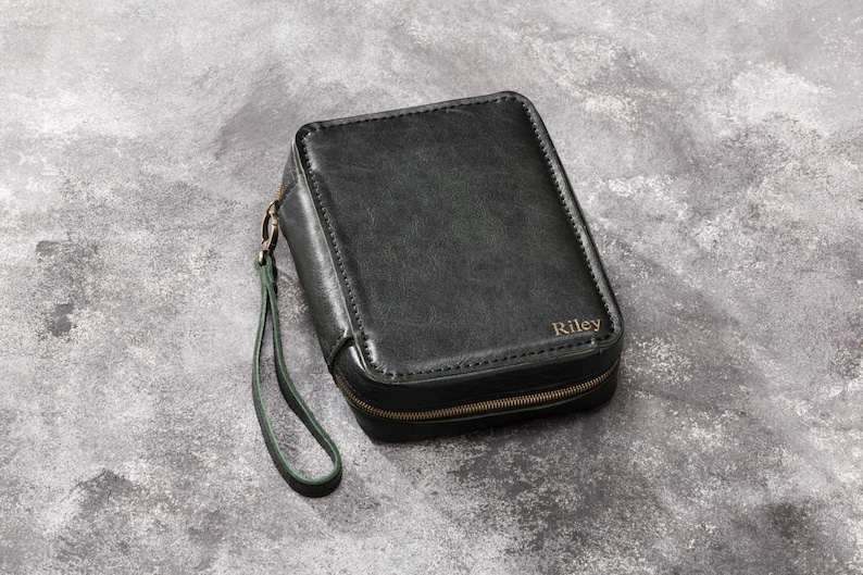 May include: A black leather zipped pouch with a green strap and the name "Riley" embossed on the front.