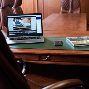 May include: A laptop computer with a green desk mat, a book titled "Houses", and a black phone on a wooden desk.