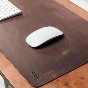 May include: A dark brown leather desk mat with a white computer mouse and keyboard. The mat has the embossed initials "R&K" in the lower right corner. The desk and mat are on a wooden surface.