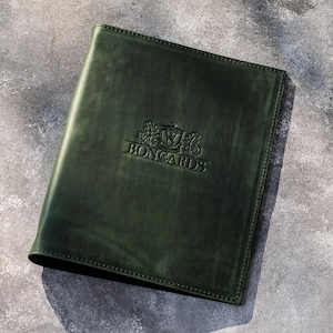 May include: A dark forest green leather folder featuring a rectangular shape with stitched edges. The front cover displays a debossed emblem with the text BONGARDS centered in the middle, surrounded by a crest design with leaf-like details.
