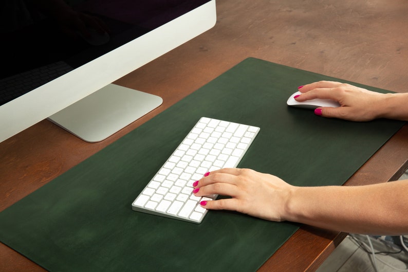 May include: A green leather desk mat with a white wireless keyboard and mouse. The keyboard and mouse are on a green desk mat.