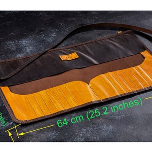 K&ouml;nnte beinhalten: Eine braune Lederrolle mit gelbem Lederinnenfutter und einem Riemen. Die Rolle ist 64 cm lang und 32 cm breit. Sie tr&auml;gt ein Etikett mit der Aufschrift "BIDA".
