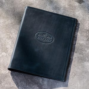 May include: A rectangular black leather menu cover featuring a debossed oval logo in the center with the text PARLOUR PARK & OAK. The cover has stitched edges and a smooth, matte finish, presenting a professional and clean appearance for document storage.