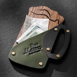 Può includere: Un portafoglio in pelle verde con manico nero e rivetti dorati, contenente una ricevuta e una banconota da 100 dollari USA. Il portafoglio presenta la scritta in rilievo "Bar Moon Design".