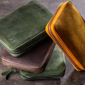 May include: Three leather zippered pouches in green, brown and yellow. The green pouch has the initials "AB" embossed on the front.