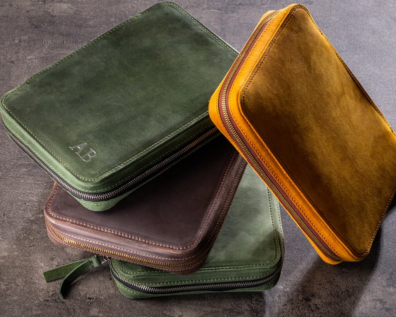 May include: Three leather zippered pouches in green, brown and yellow. The green pouch has the initials "AB" embossed on the front.