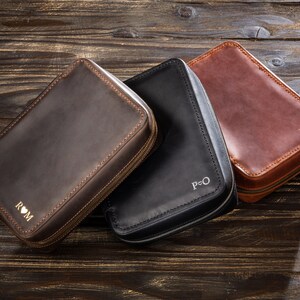 May include: Three leather zippered pouches with personalised initials. The pouches are brown, black, and dark brown. The initials are "ROM", "P&O", and "B+K".