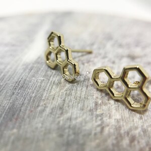 May include: A pair of gold honeycomb-shaped stud earrings. The earrings are made of metal and have a simple, geometric design.