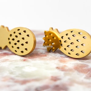 Könnte beinhalten: Ein Paar goldfarbene Ohrstecker in Ananasform. Die Ohrringe sind aus Metall und haben ein detailliertes Design.