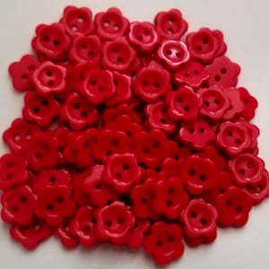Könnte beinhalten: Ein großer Haufen roter, plastikblumenförmiger Knöpfe mit jeweils zwei Löchern.