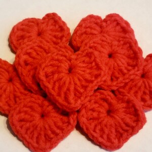 Op de afbeelding: Een groep van zeven gehaakte rode harten. De harten zijn gemaakt met een textuur-steek en zijn allemaal even groot.