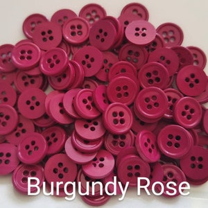 Pode incluir: Um grande monte de botões cor de rosa bordô. Os botões são todos do mesmo tamanho e têm quatro furos.