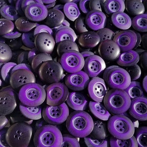 May include: A large group of purple buttons with four holes each. The buttons are made of a shiny, smooth material and have a slight iridescent sheen.