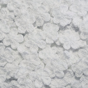 May include: A close-up of a pile of white crocheted flowers. The flowers are small and delicate, and they are perfect for adding a touch of handmade charm to any project.