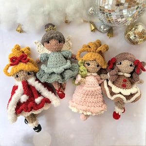 May include: Four handmade crochet dolls in various outfits. One doll wears a red and white coat, another a blue dress, a third a pink dress, and the last a brown dress. Each doll has a unique hairstyle and facial features, with small details like bows and wings.