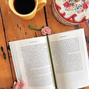 May include: A close-up of an open book with a pink flower bookmark. The book is titled "Fast Like a Girl" and the text on the page discusses the "Fasting Cycle". A cup of coffee and a decorative tin box are visible in the background.