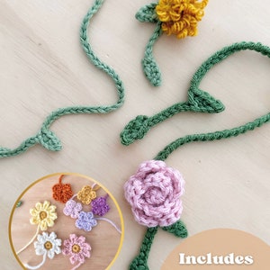 May include: Four crocheted flowers in pink, yellow, orange, and purple with green stems. The flowers are arranged in a circle with a white background. The text "Includes 4 Crochet Flowers for Bookmark Vines & Paper Clips" is in the lower right corner of the image.