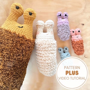 Pode incluir: Cinco brinquedos de amigurumi de crochê em forma de caracol, em várias cores e texturas. Os caracóis estão dispostos numa superfície de madeira. O caracol maior é castanho e tem uma textura felpuda. Os outros caracóis são mais pequenos e têm uma variedade de cores e texturas, incluindo branco, roxo e rosa. A imagem inclui o texto "Pattern Plus Video Tutorial".