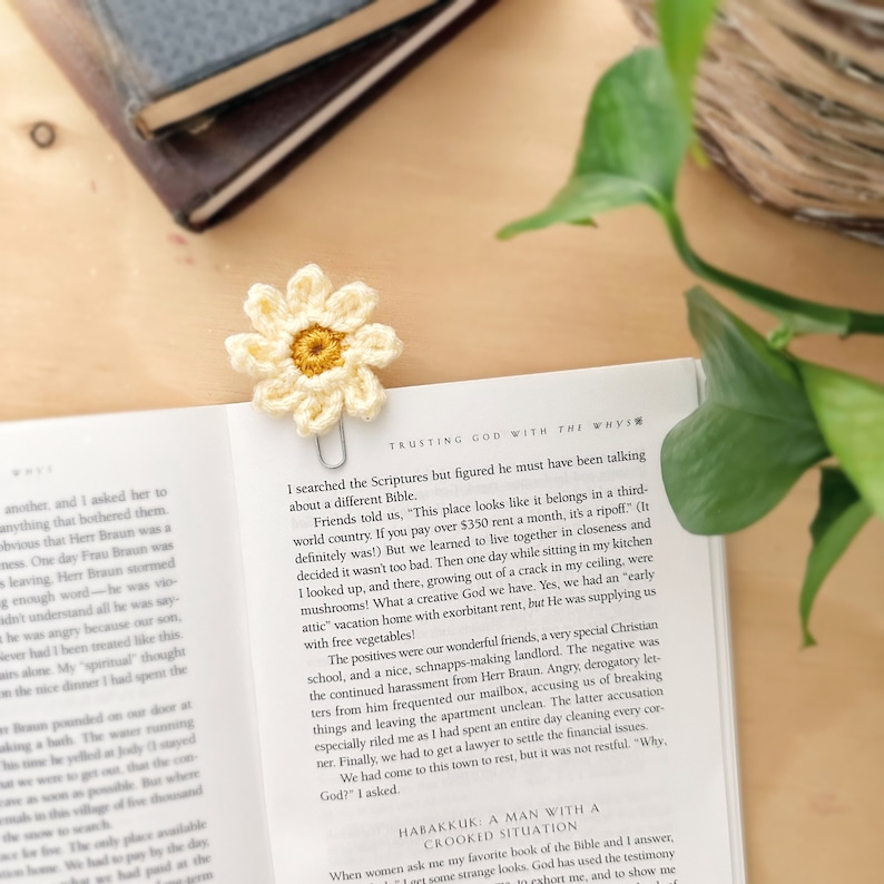 May include: A close-up of a book with a crocheted daisy bookmark. The book is open to a page with the text "TRUSTING GOD WITH THE WHYS" and a passage about a family's struggles with their landlord.