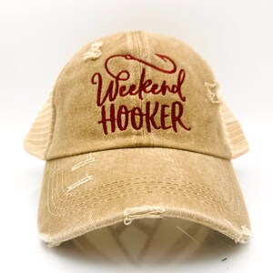 May include: A brown distressed baseball cap with a red embroidered design that says "Weekend Hooker" with a fishing hook above the text.