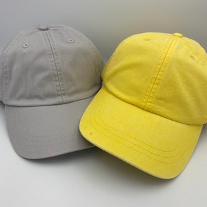 May include: Two baseball caps, one grey and one yellow. Both caps have a classic design with a curved brim.