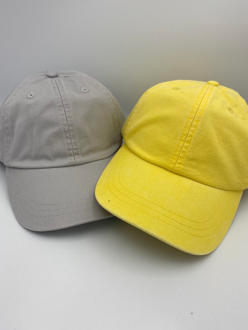May include: Two baseball caps, one grey and one yellow. Both caps have a classic design with a curved brim.