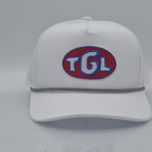 Peut inclure: Casquette de camionneur blanche avec une visi&egrave;re incurv&eacute;e et un dos en filet. L'avant pr&eacute;sente un &eacute;cusson ovale brod&eacute; avec les lettres "TGL" en blanc, soulign&eacute;es de bleu, sur fond rouge. Un d&eacute;tail de corde noire et blanche orne la visi&egrave;re.