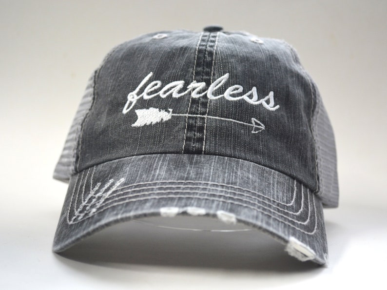 May include: A black and gray distressed trucker hat with a white embroidered arrow and the word "fearless".