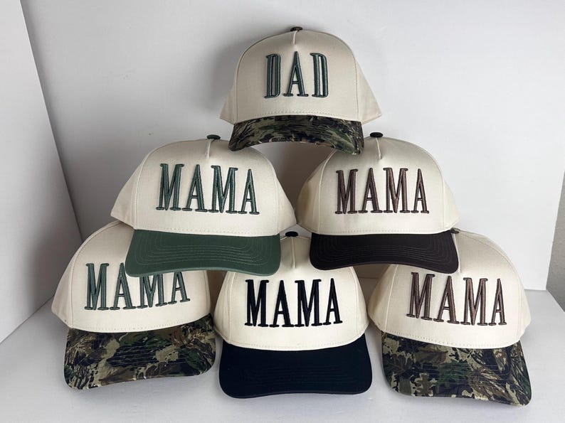 May include: Cream-colored baseball caps with the words "DAD" and "MAMA" embroidered in dark green and brown. The caps have different colored brims, including camouflage, dark green, and black.