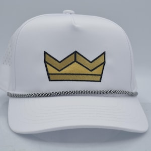 Peut inclure: Casquette de baseball blanche orn&eacute;e d'une couronne dor&eacute;e. La casquette est dot&eacute;e d'une visi&egrave;re incurv&eacute;e, d'un cordon noir et blanc et de petits trous d'a&eacute;ration. Un accessoire &eacute;l&eacute;gant pour se prot&eacute;ger du soleil.