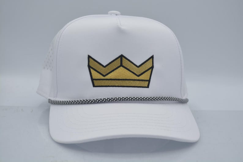 Peut inclure: Casquette de baseball blanche orn&eacute;e d'une couronne dor&eacute;e. La casquette est dot&eacute;e d'une visi&egrave;re incurv&eacute;e, d'un cordon noir et blanc et de petits trous d'a&eacute;ration. Un accessoire &eacute;l&eacute;gant pour se prot&eacute;ger du soleil.