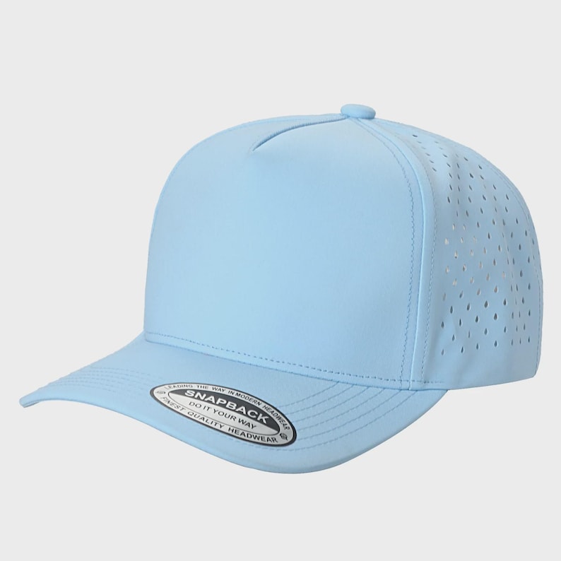 May include: A light blue five-panel snapback cap with laser-cut ventilation holes on the side panels. The brim features a circular sticker with the text: LEADING THE WAY IN MODERN HEADWEAR SNAPBACK DO IT YOUR WAY FINEST QUALITY HEADWEAR.