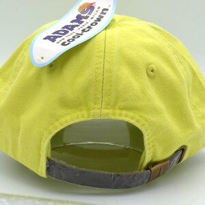 May include: Back view of a yellow baseball cap with a brown adjustable strap. The cap has a label attached to the back that reads "Adams CoolCrown".