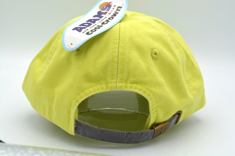 May include: Back view of a yellow baseball cap with a brown adjustable strap. The cap has a label attached to the back that reads "Adams CoolCrown".