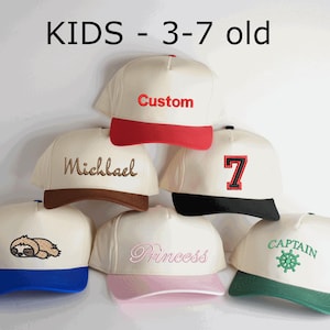 May include: A collection of cream-colored baseball caps with various colored brims, including red, brown, black, blue, pink, and green. Each cap features embroidered text or a graphic, such as "Custom," "Michael," "7," "Princess," "Captain," and a sloth.