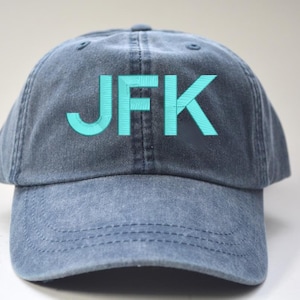 May include: A blue denim baseball cap with a turquoise embroidered "JFK" logo.