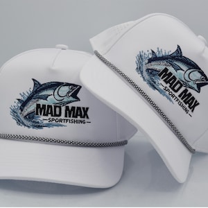 Peut inclure: Deux casquettes de baseball blanches avec un motif de poisson brod&eacute; noir et bleu et le texte "MAD MAX - SPORTFISHING". Chaque casquette a un d&eacute;tail de corde noir et blanc autour du bord.