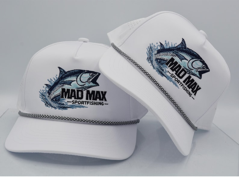 Peut inclure: Deux casquettes de baseball blanches avec un motif de poisson brod&eacute; noir et bleu et le texte "MAD MAX - SPORTFISHING". Chaque casquette a un d&eacute;tail de corde noir et blanc autour du bord.