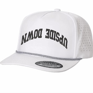May include: White snapback hat with the words "UPSIDE DOWN" in black, arched across the front. The hat has a perforated side panel and a black and white rope detail along the brim. A black tag with white text is on the brim.