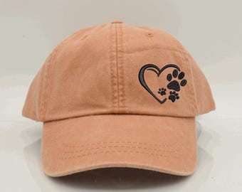 May include: A light brown baseball cap with a black embroidered heart and paw prints. The heart is outlined in black and has three paw prints inside.