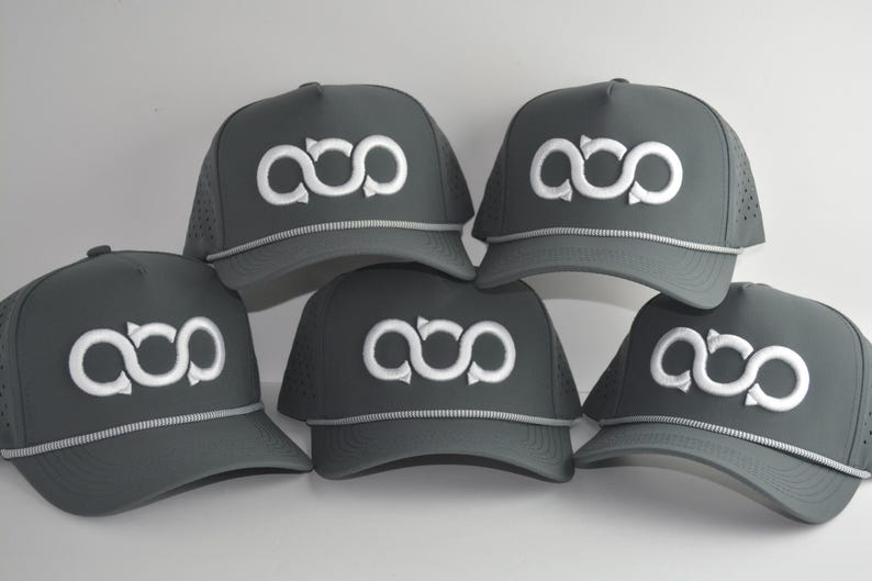 May include: Five dark grey baseball caps arranged in a group. Each cap features a white embroidered infinity-style logo on the front panel, a light grey rope detail across the base of the crown, and perforated side panels for ventilation.