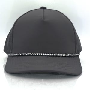 May include: A solid dark grey baseball cap featuring a five-panel construction with a structured crown and a curved brim. A decorative, reflective silver and black braided cord trim runs horizontally across the base of the front crown panel.