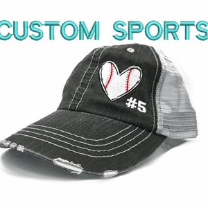 May include: A black and white baseball cap with a distressed look. The cap has a white mesh back and a black front with a white heart embroidered on it. The heart has a baseball stitched inside of it and the number 5 below it.