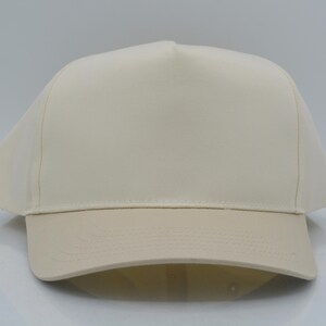 May include: A cream-colored baseball cap with a structured crown and a curved brim. The cap is made of a solid, neutral-toned fabric, suitable for various outfits. The brim is a slightly darker shade of cream.