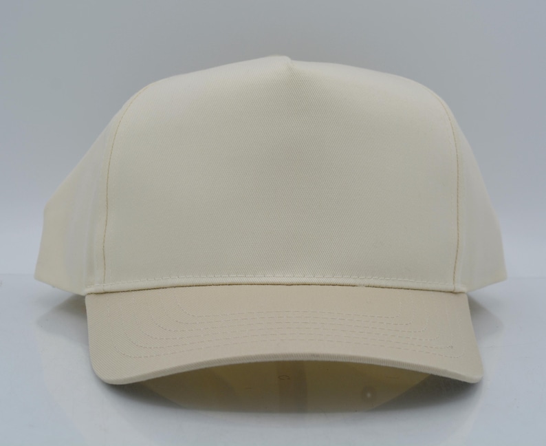 May include: A cream-colored baseball cap with a structured crown and a curved brim. The cap is made of a solid, neutral-toned fabric, suitable for various outfits. The brim is a slightly darker shade of cream.